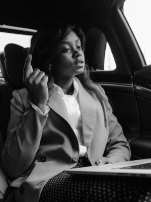 Black and white photo of a businesswoman working on a laptop in the car's backseat, poised and professional.